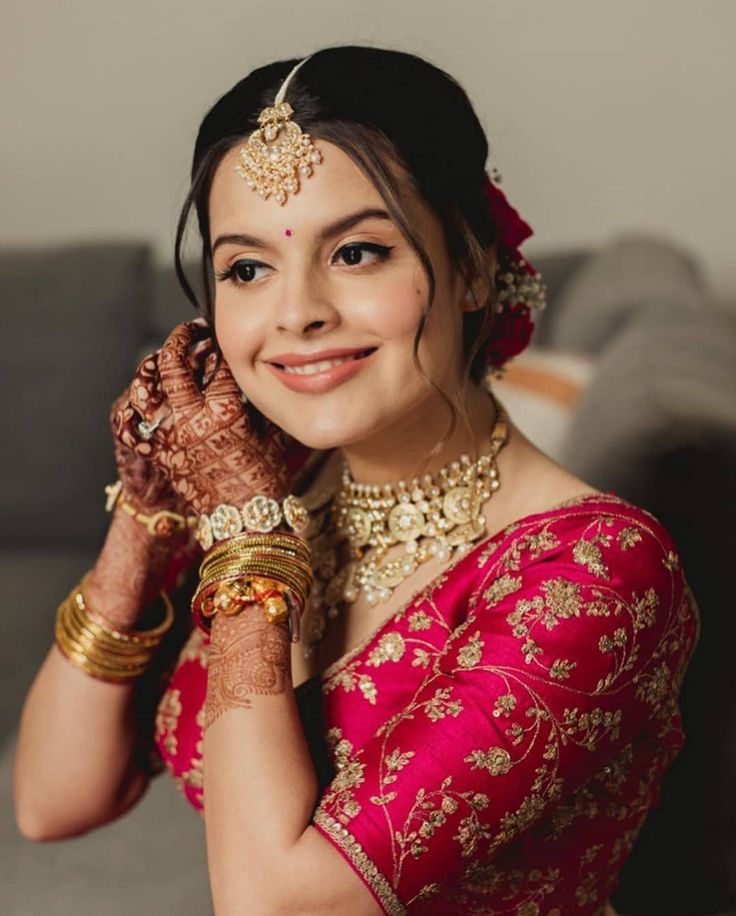 a woman in a red and gold sari with her hands on her chest, smiling