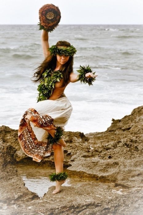 a woman with flowers in her hair dancing on the rocks by the water's edge