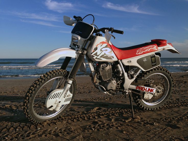 a red and white dirt bike parked on top of a beach next to the ocean