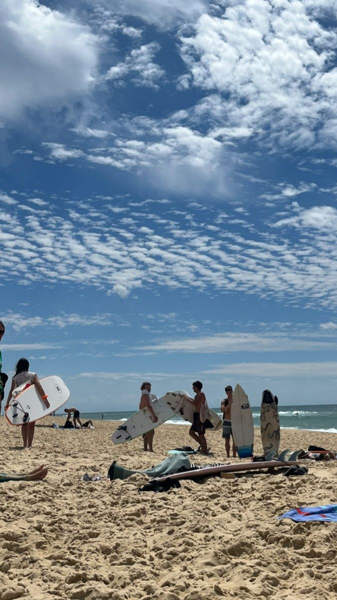 several people on the beach with surfboards under a blue sky filled with white clouds