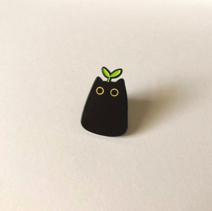 a small black object with a plant growing out of it's head on a white surface