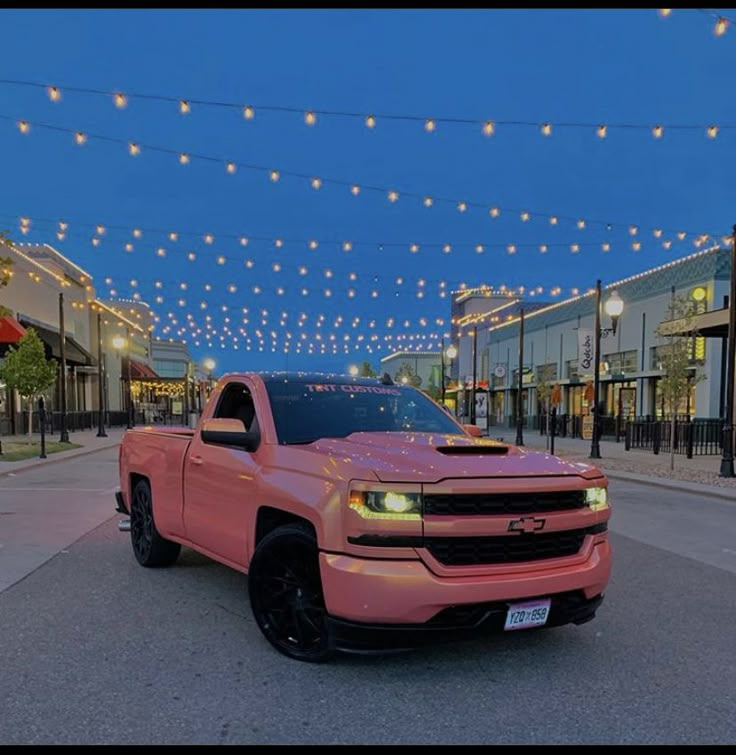 a pink truck parked in front of a building with christmas lights strung across the street