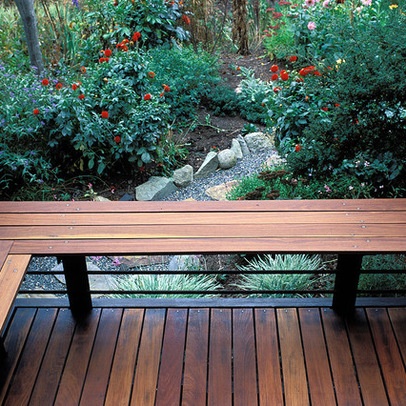 a wooden bench sitting on top of a wooden deck next to bushes and flowers in the background