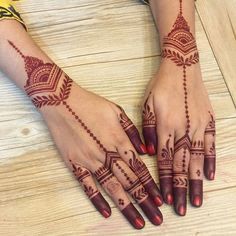 two hands with henna designs on them sitting on a wooden table next to each other