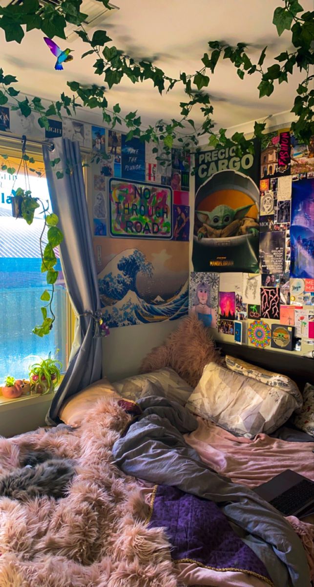 an unmade bed sitting in front of a window covered with posters and plants on the wall