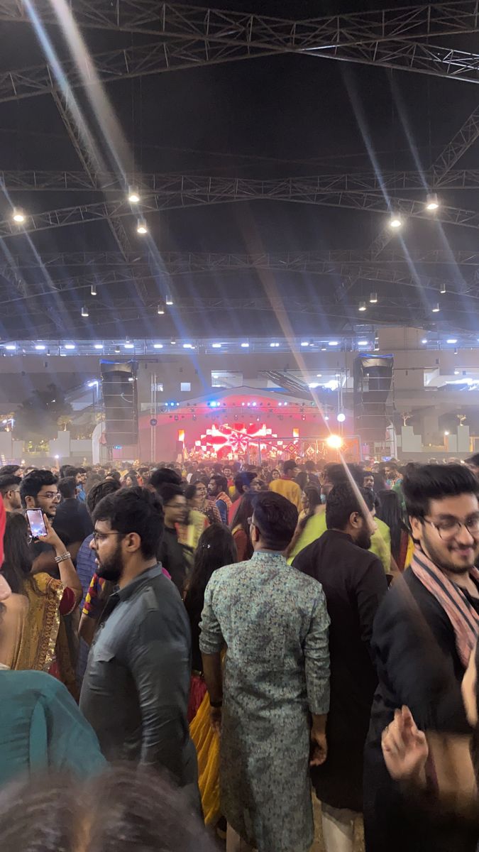 a large group of people standing around in front of a stage with lights on it