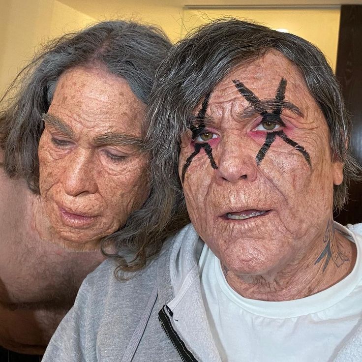 two older people with faces painted to look like they have crosses on their foreheads