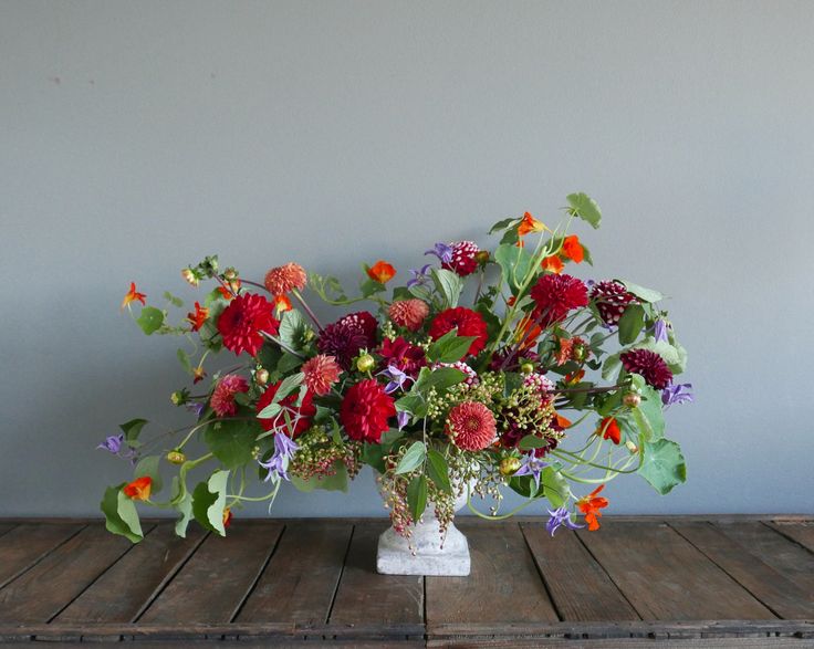 a vase filled with lots of colorful flowers on top of a wooden table next to a wall