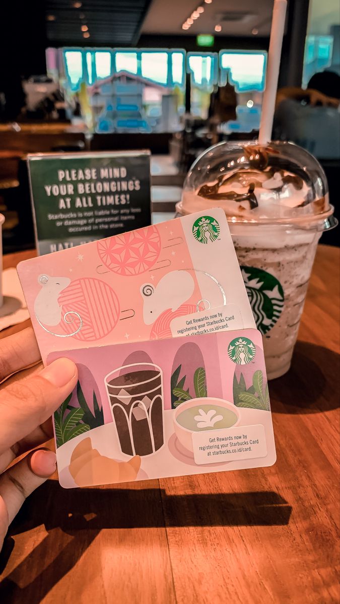 someone holding up a starbucks card at a table