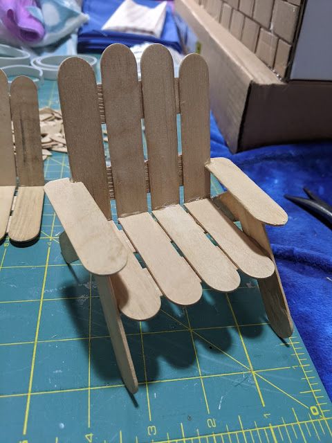 two wooden chairs sitting on top of a blue cutting mat next to a ruler and scissors