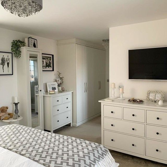 a bedroom with white furniture and a flat screen tv mounted on the wall above it