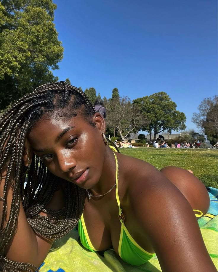 a woman laying on top of a towel in the grass with her hair braided