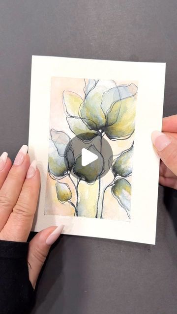 two hands holding up a card with watercolor flowers on it and the video below