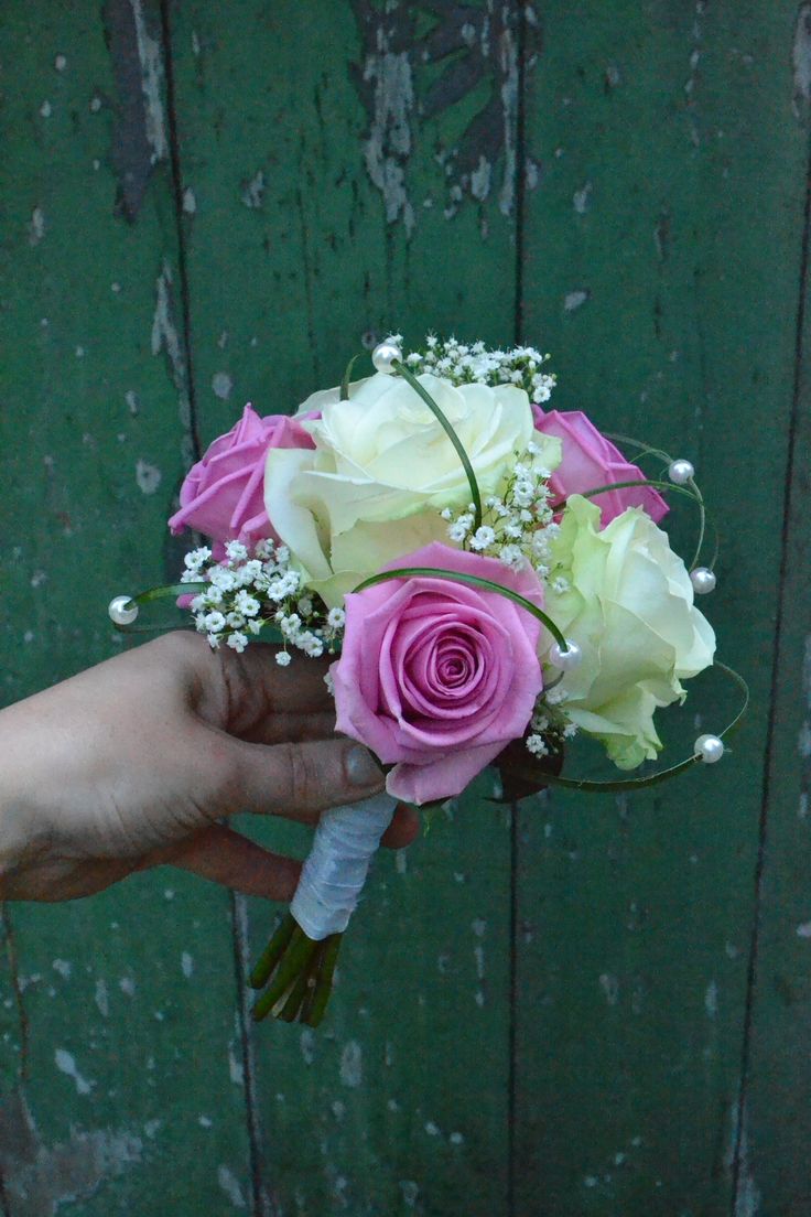 a person holding a bouquet of pink and white flowers in their hand on a wooden background