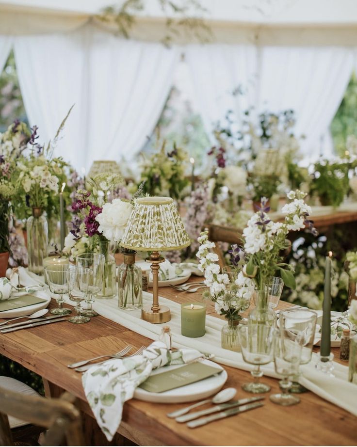 the table is set with flowers, candles and place settings for an outdoor dinner party