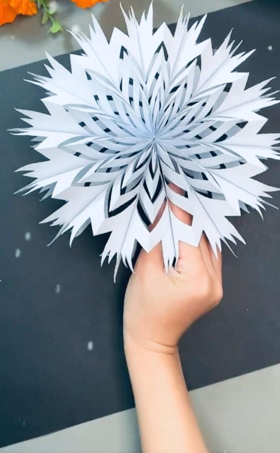 someone is holding up a paper snowflake that looks like an origami flower