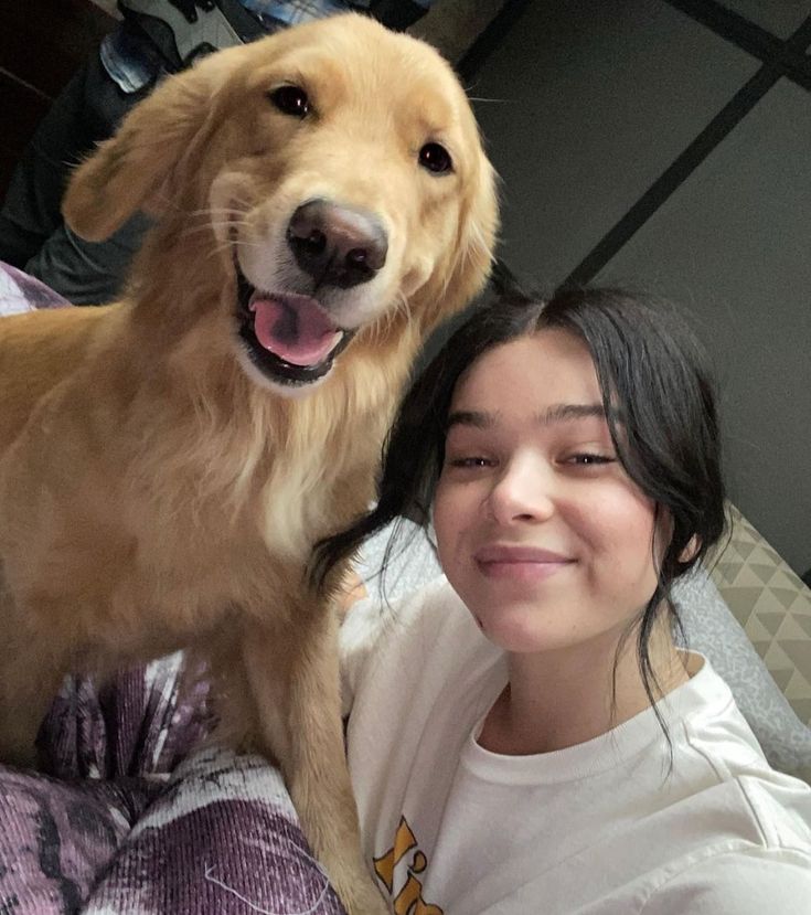 a woman sitting next to a large brown dog on top of a bed in front of her