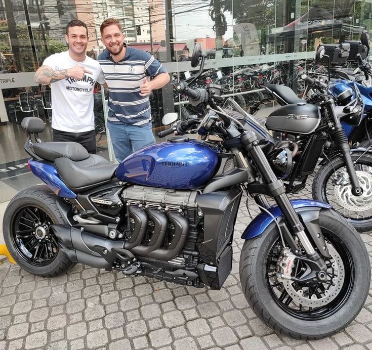 two men standing next to motorcycles in front of a building