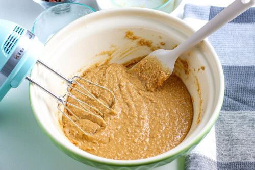 a mixing bowl filled with peanut butter and whisk next to an electric mixer