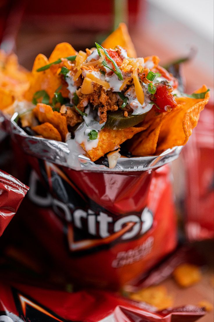 a red bag filled with nachos sitting on top of a wooden table next to chips