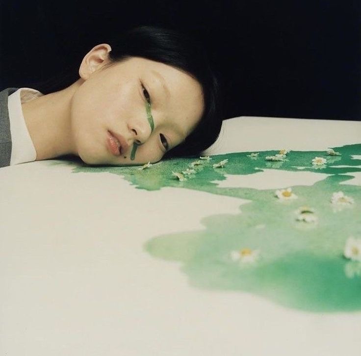 a woman laying on top of a bed with her head resting on a green leaf