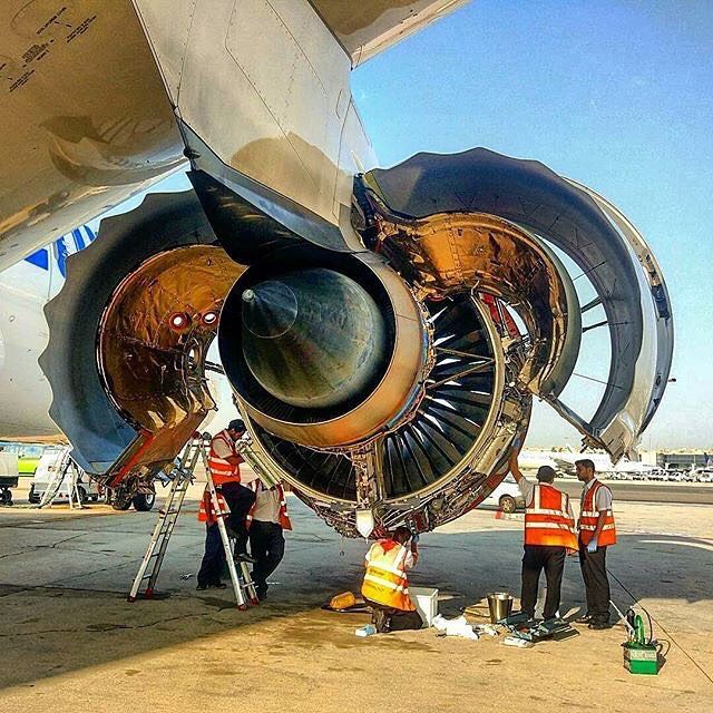 men in orange vests standing next to an airplane engine