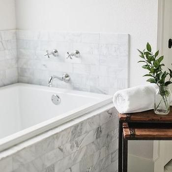 a white bath tub sitting next to a wooden table with a vase on top of it