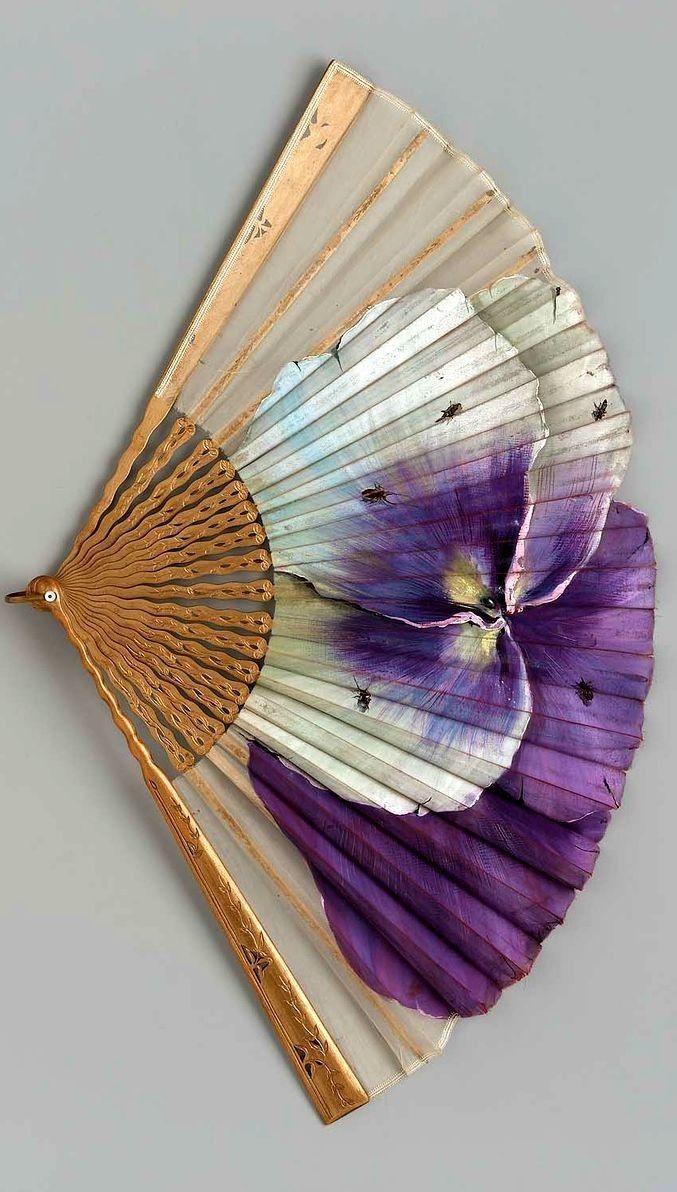 a purple and white flower on top of a wooden fan with gold trimmings