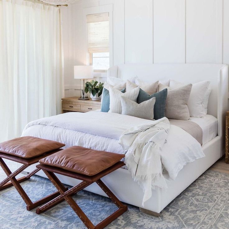 a white bed sitting in a bedroom next to a wooden table with two stools