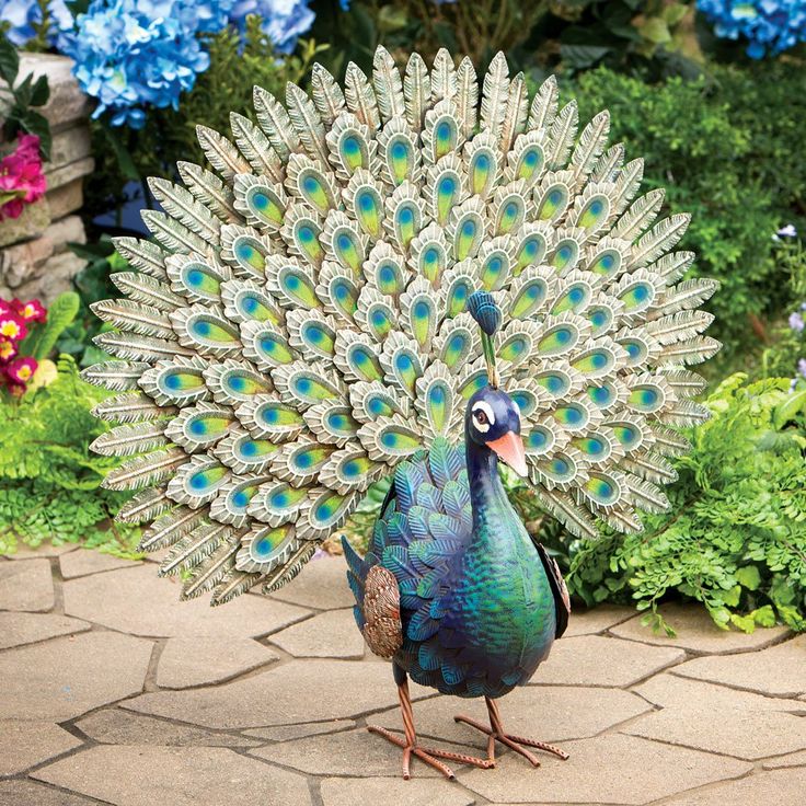 a peacock standing on top of a stone walkway next to flowers and bushes with its feathers spread out