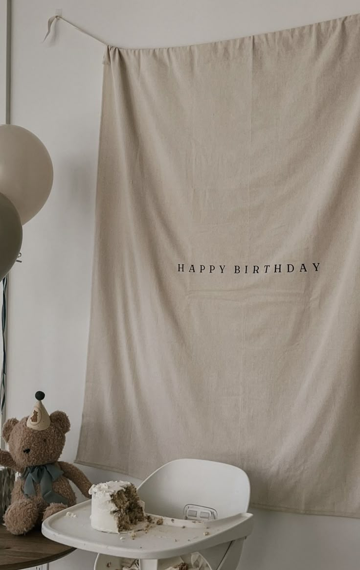 a teddy bear sitting in front of a birthday cake on a table next to balloons