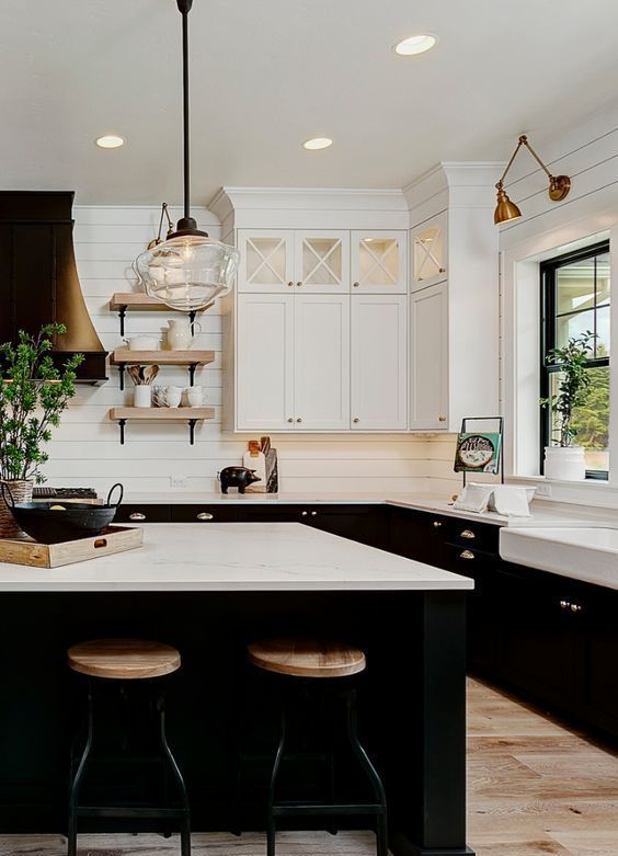 a kitchen with black and white cabinets, an island in the middle and two stools at the end