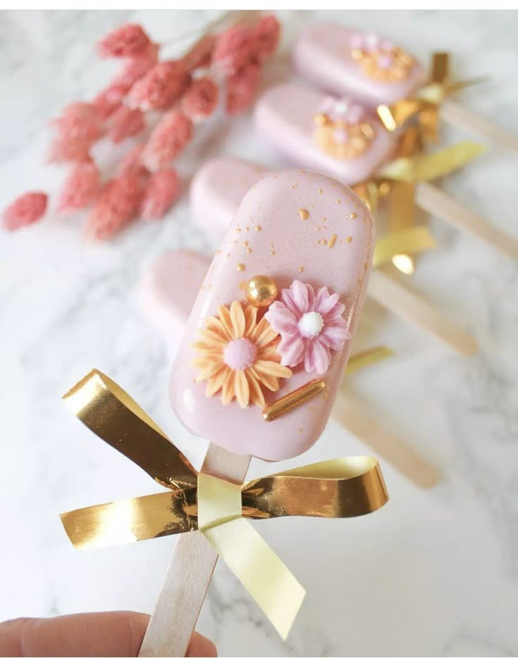 a hand holding a lollipop with pink and gold decorations on top of it