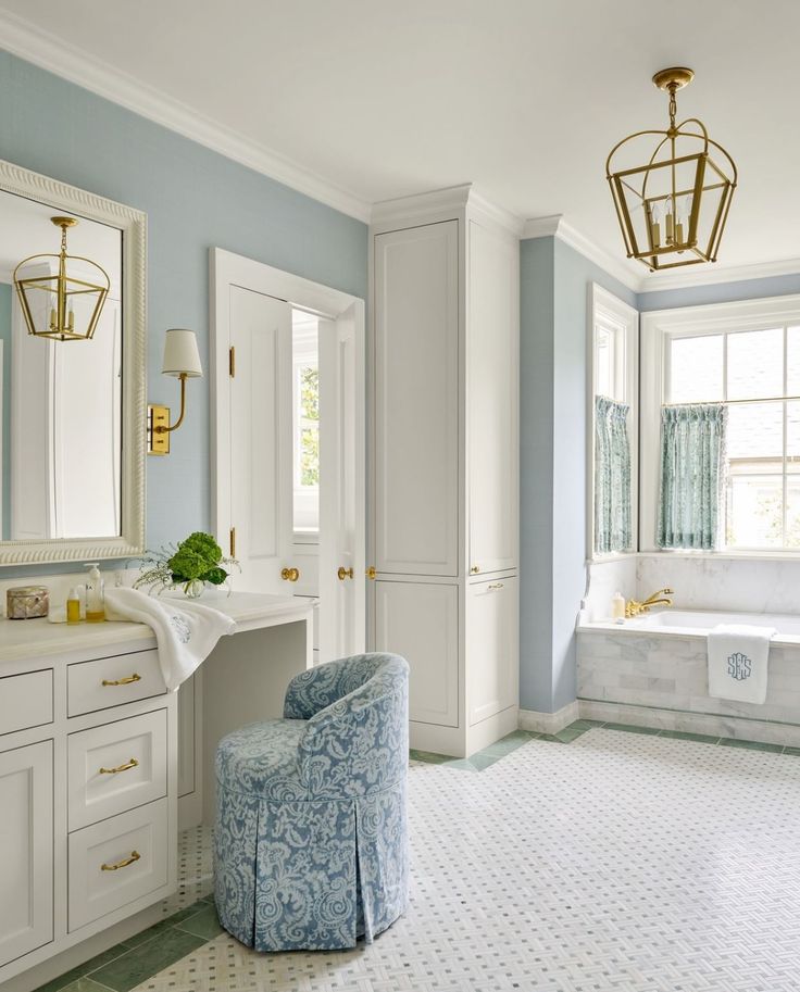 a blue and white bathroom with a tub, sink, mirror and chair in it