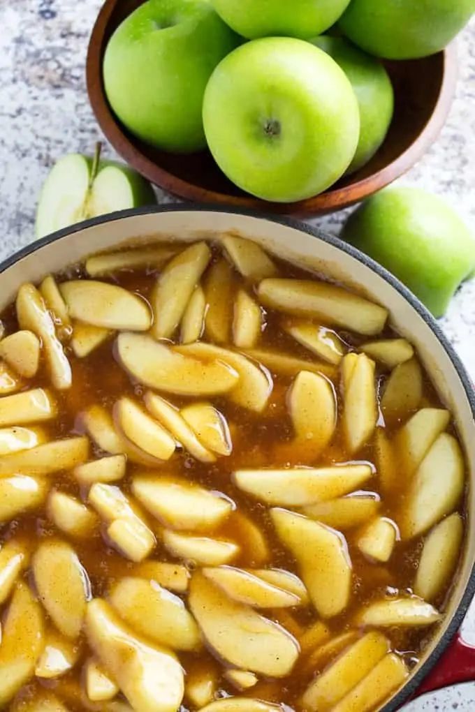 an apple pie with apples in the background and two bowls full of apples next to it