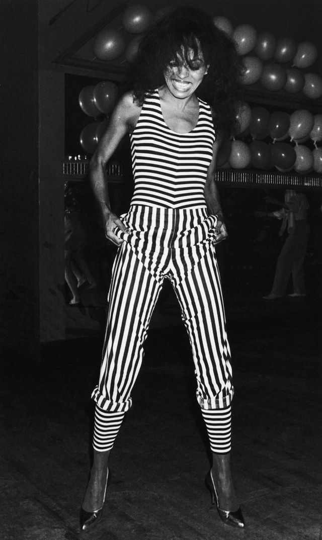 a black and white photo of a woman in striped pants with her hands on her hips