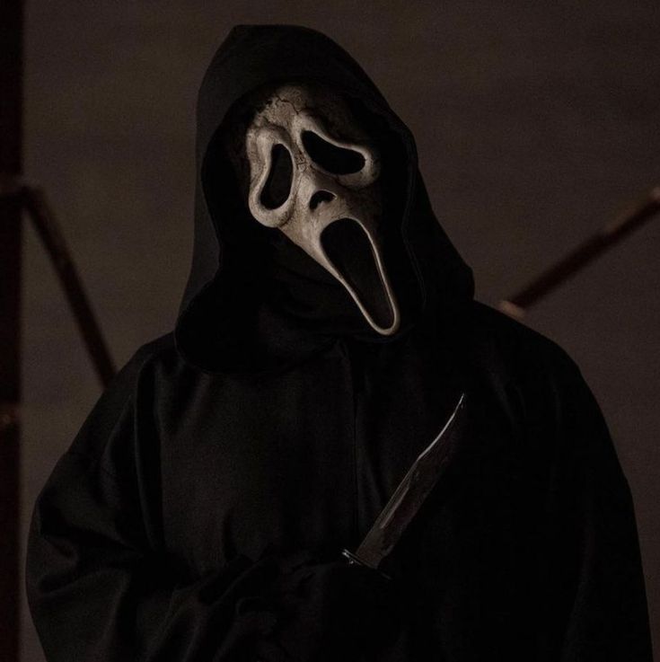 a man in a black hooded jacket holding a knife and wearing a ghost mask with his mouth open