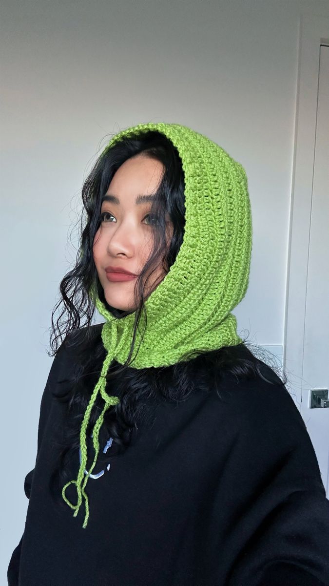 a woman wearing a green knitted hoodie and black top with her hair in the wind