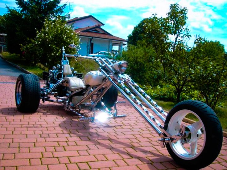 an unusual motorcycle is parked on the side of a brick road in front of a house