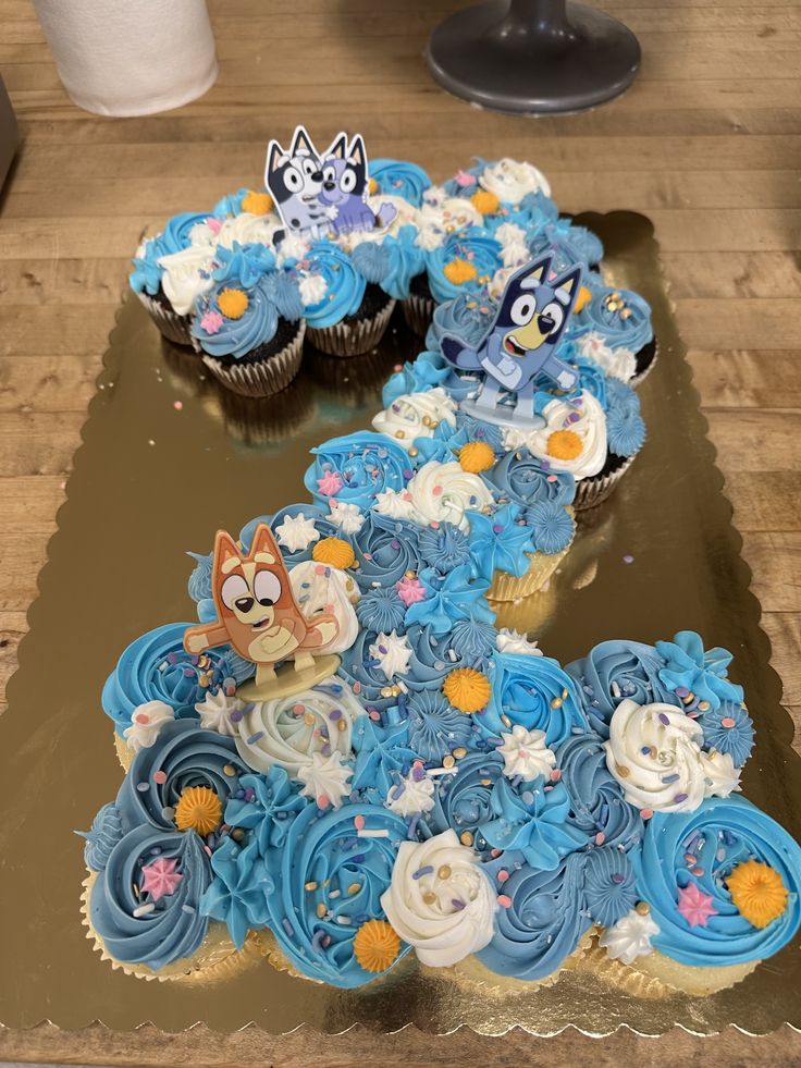 two cupcakes with blue frosting on top of a wooden table next to each other