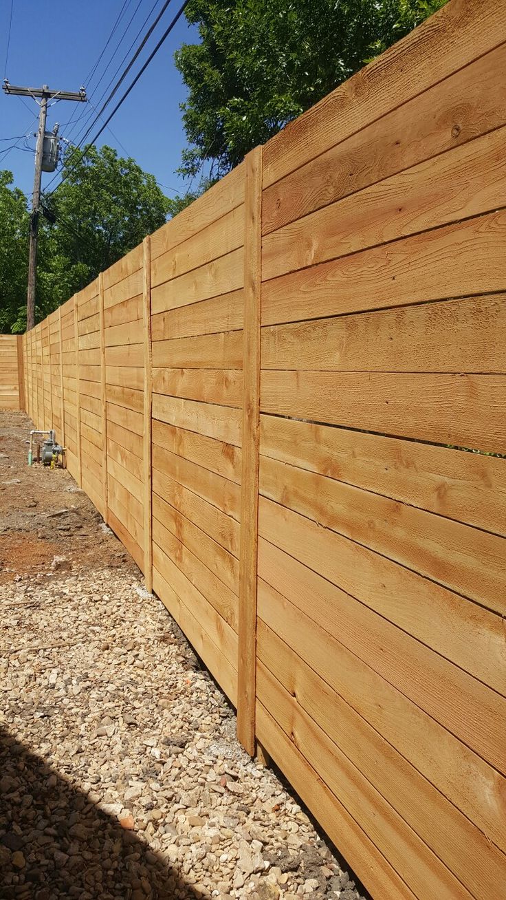 a wooden fence that is next to some gravel and trees in the background with power lines above it