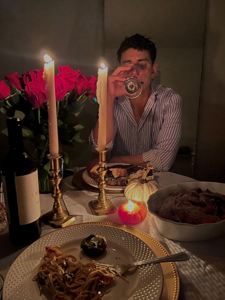 a man sitting at a table in front of a plate with spaghetti and two candles