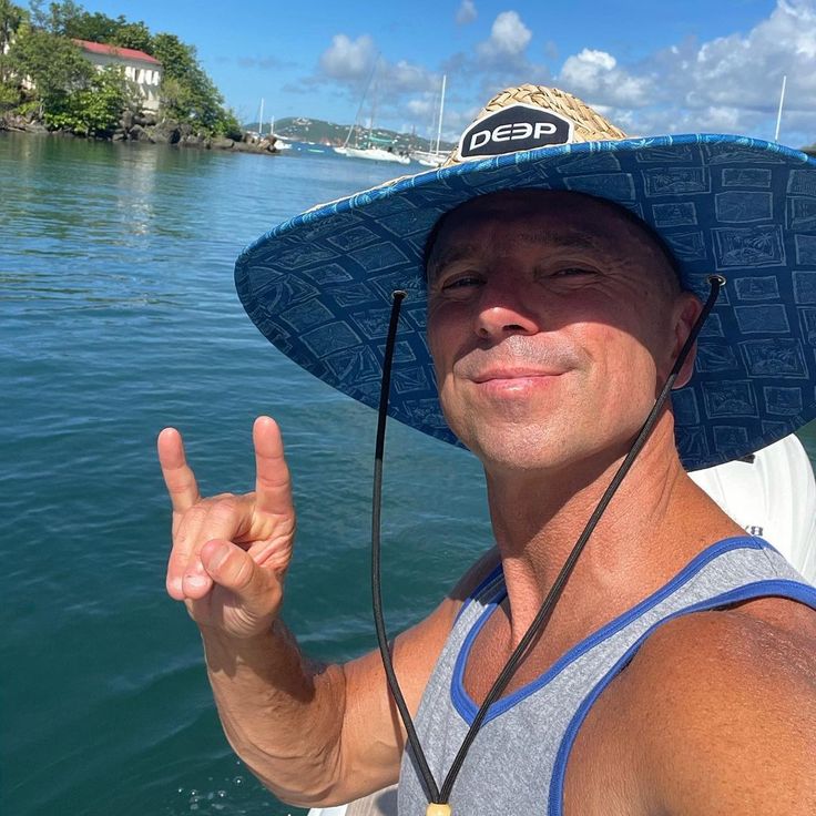 a man on a boat wearing a hat and making the peace sign with his hand