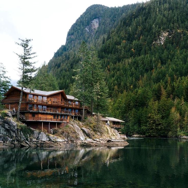 a wooden house sitting on top of a lush green hillside next to a body of water