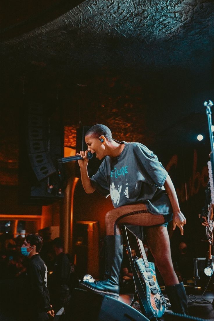 a woman standing on top of a bike while holding a microphone in her hand and singing into a mic