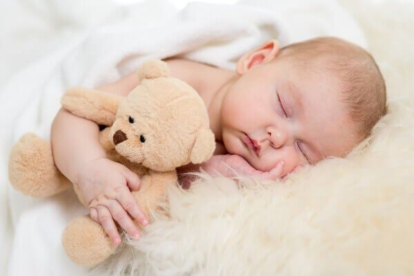 a baby sleeping next to a teddy bear on top of a white blanket with it's eyes closed