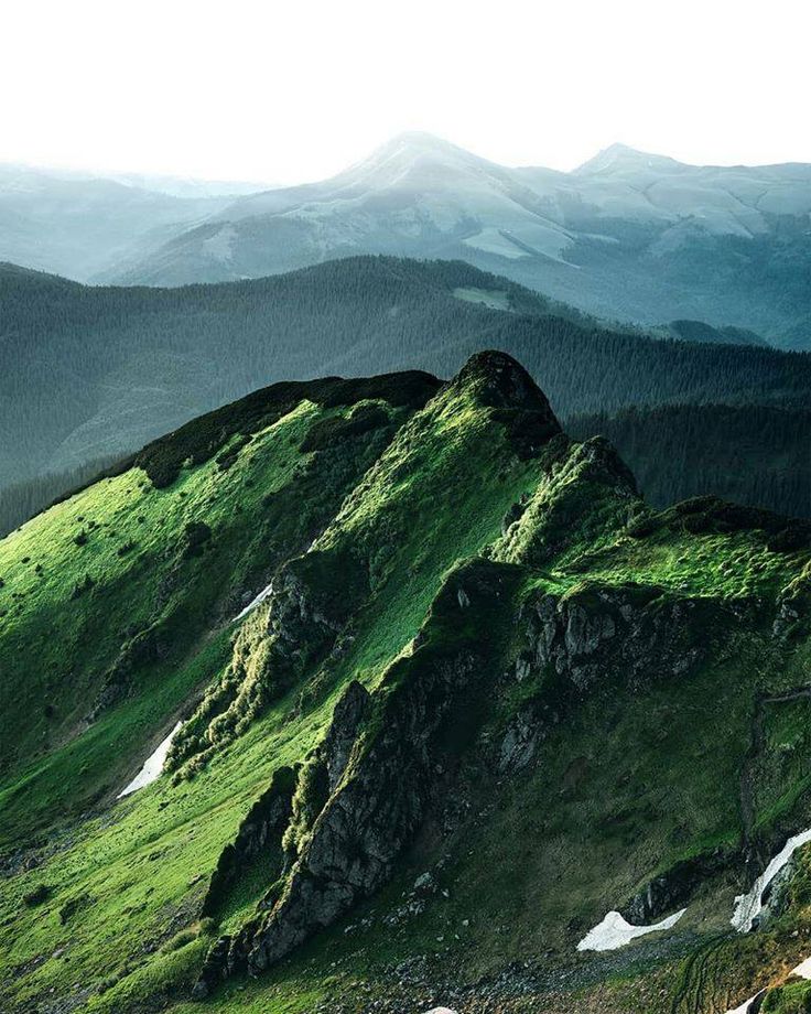 a green mountain covered in lots of grass and rocks with mountains in the back ground