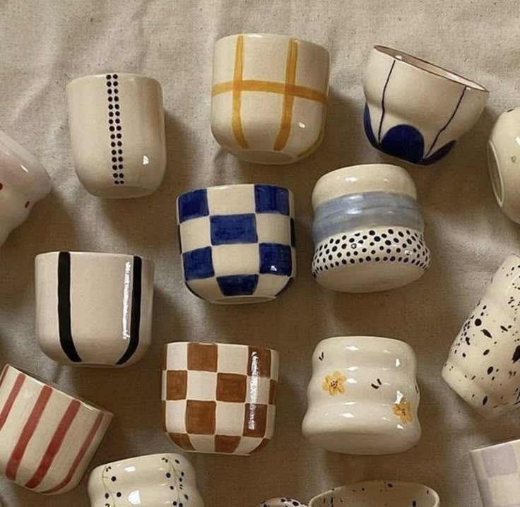 many different colored cups and bowls on a white tablecloth, all lined up in the same pattern