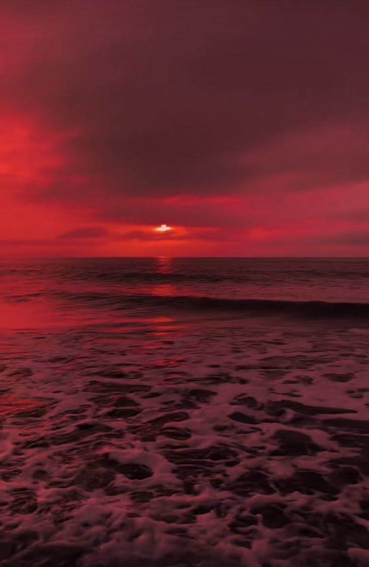 the sun is setting over the ocean with waves coming in to shore and red clouds