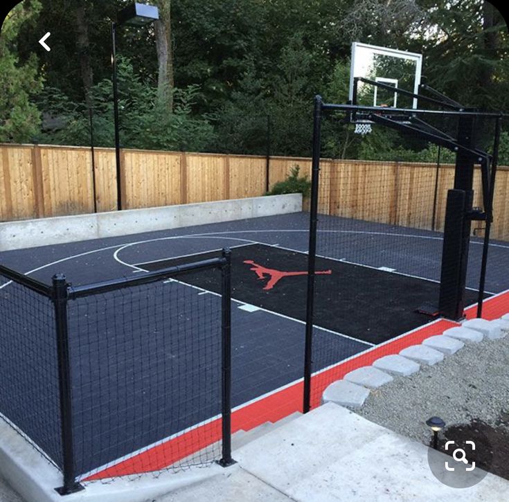 an outdoor basketball court in the middle of a fenced in area with a basketball hoop